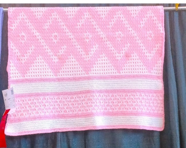 A pink and white baby blanket with diamond pattern